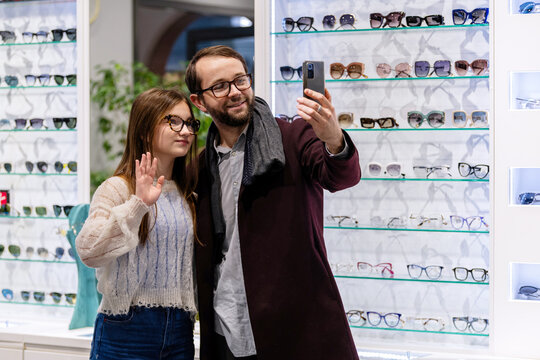 Father and daughter taking selfie with smartphone in optician store.