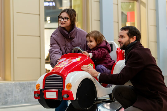 Father and Teen Sister Watching Child Riding Arcade Car