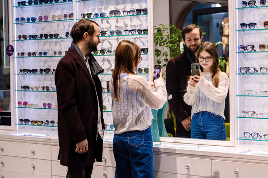 Father and daughter choosing glasses frames in optician shop.