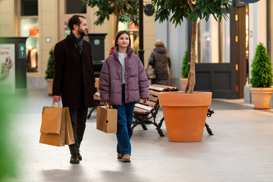 Father and Teenage Daughter Walking in Shopping Mall with Bags