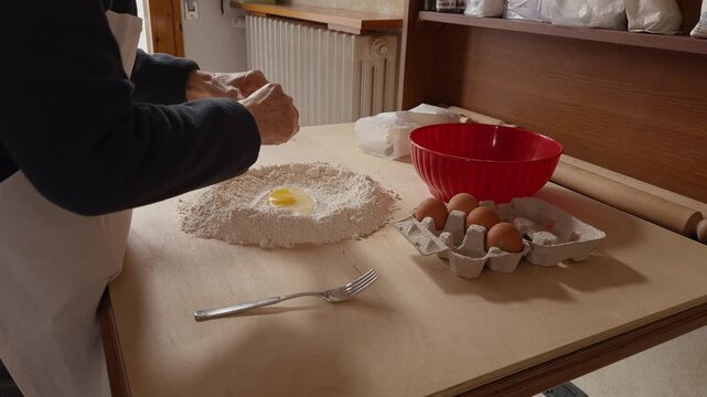 Traditional Romagna cook cracks eggs into flour to prepare fresh cappelletti dough on a wooden table. Authentic Italian pasta-making process in a rustic kitchen.