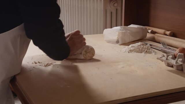 Side view of a Romagna cook hand-kneading fresh cappelletti dough on a wooden table. Traditional Italian pasta-making in a home kitchen with simple tools and ingredients.