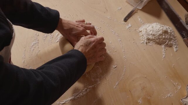 Top view of a Romagna cook finishing fresh cappelletti dough by hand and dropping it onto a wooden table. Traditional Italian pasta-making with flour traces and rustic tools.