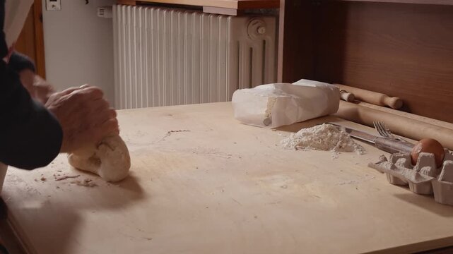 Side view of a Romagna cook kneading fresh cappelletti dough by hand on a wooden table. Traditional Italian pasta-making in a cozy home kitchen with simple tools and ingredients.