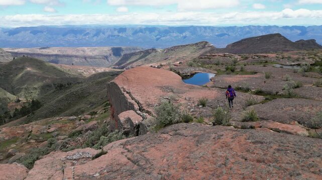 Aerial tracks woman running to edge of tall sandstone cliff in Bolivia