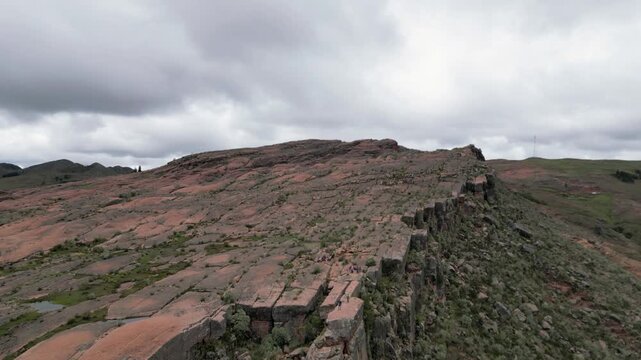 Aerial pulls out from people atop tall sandstone escarpment cliff