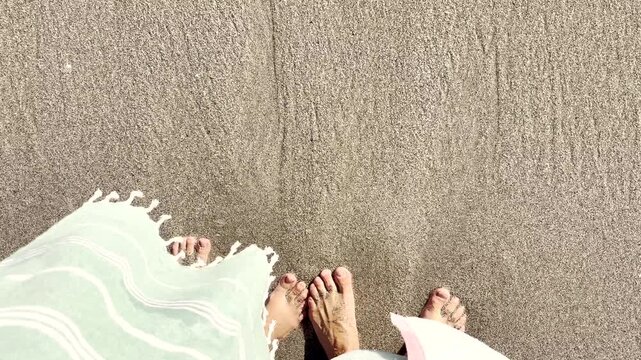 Top view of couple on wet beach sand wriggling toes as wave rolls in