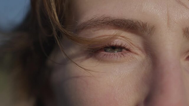 Woman blue eye opening and squinting in bright sunlight with hair movement