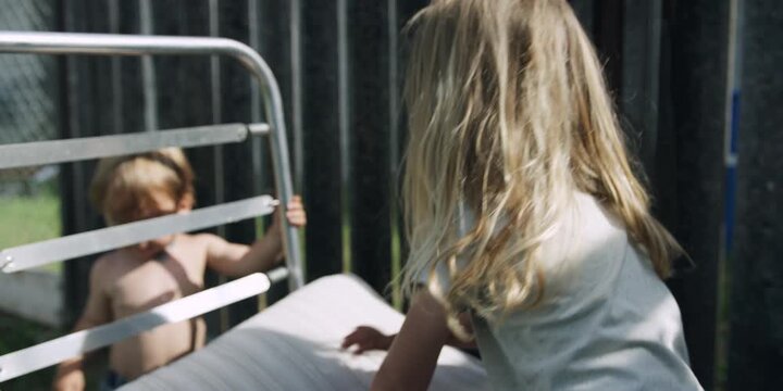 Toddler peering through a sun lounger frame at his sibling