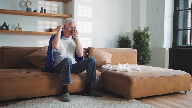 Sick old man breathing through nebulizer at home, therapeutic inhalation. Recovery of lung health after covid or pneumonia, rehabilitation of respiratory tract during influenza disease, senior man