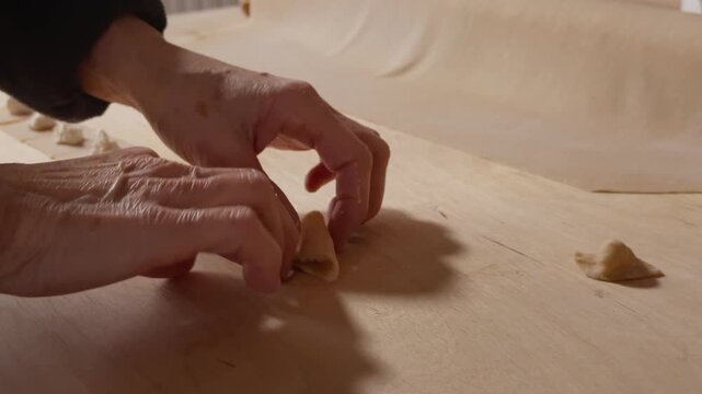 Elderly hands gently folding filled pasta on a wooden surface, highlighting the precision of homemade preparation.