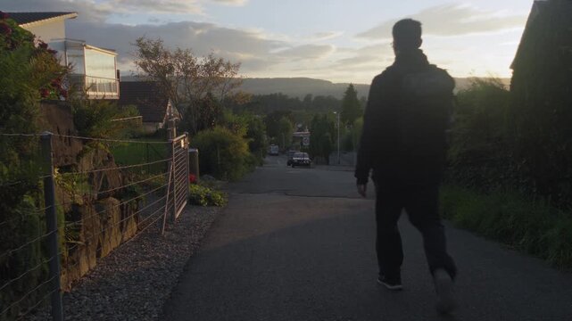 Man with a backpack walking down a street with trees at sunset in late summer