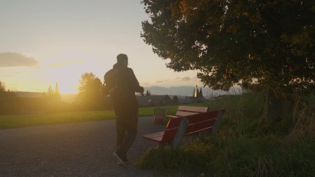 Young man with a backpack sits down on a bench to enjoy the sunset view, Switzerland