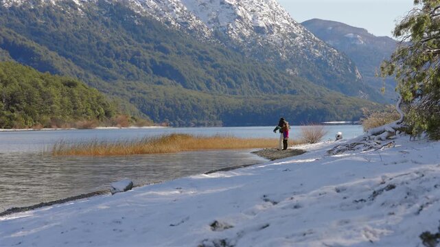 A mother and daughter enjoy stone skipping on a snowy lake shore in Patagonia, Argentina, framed by the majestic Andes mountains, bonding concept.