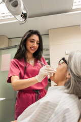 Female dentist wearing pink scrubs and gloves performing an oral examination on a patient in a modern dental clinic