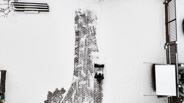 Overhead horizontal view of a person shoveling snow, clearing a narrow path upward through white ground.