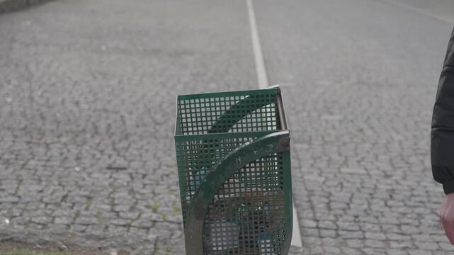 Hand collecting litter from ground and disposing it in a public bin