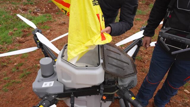 Farmers fill the solids tank of an agricultural drone with granulated urea for wheat field fertilization
