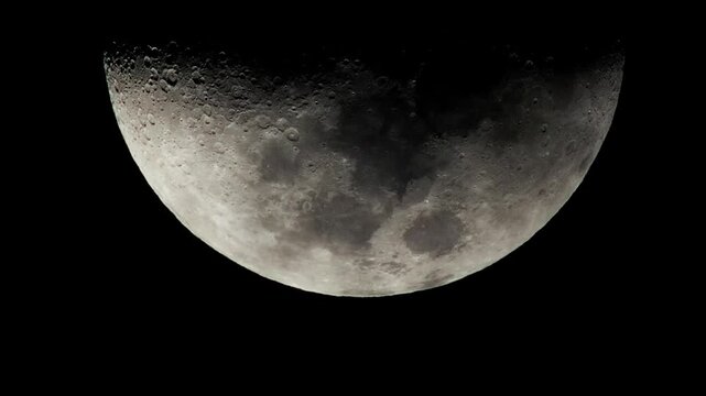A close-up shot of the moon's surface, revealing craters and dark patches. The moon appears in a crescent phase against a black background.