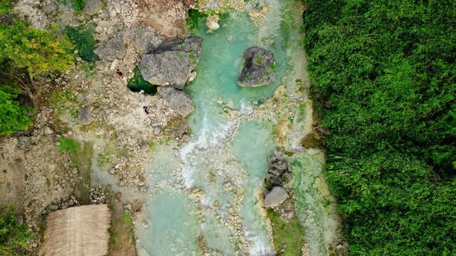 Metadata
Cinematic tilt-down and rising aerial of Bolinao Falls in Pangasinan, Philippines showing the intricate rocky textures of the vibrant turquoise riverbed below.