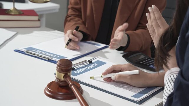 Close-up of lawyers discussing and signing a contract at a desk with gavel, clipboard, calculator and documents, suggesting legal consultation, agreement, or court settlement.