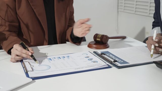 Business meeting with contract signing and financial charts on desk, hands discussing terms beside a gavel, concept of legal agreement, arbitration, corporate law and negotiation.
