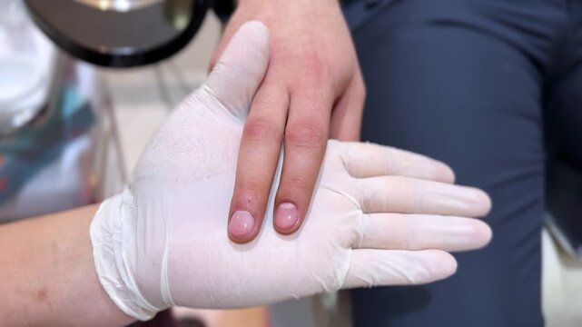 Macro shot of gloved beautician holding client&rsquo;s hand to inspect clean polished nails after manicure. Professional spa hygiene and nail treatment in salon setting.