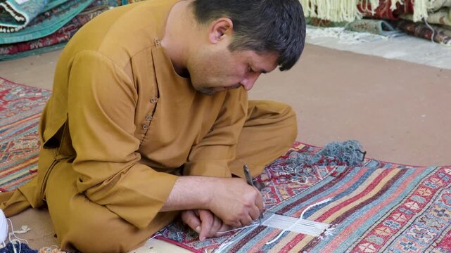 An artisan man is using traditional methods to enhance the timeless charm of vintage rugs in intricate detail. Kabul, Afghanistan
