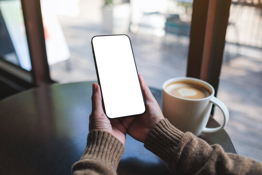 Mockup image of a woman holding mobile phone with blank desktop screen in cafe