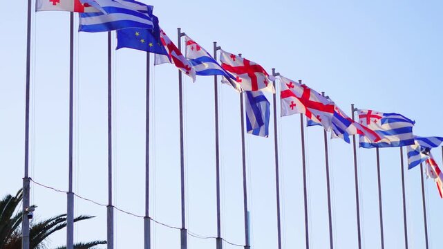 Flags of various countries waving in the wind against a clear blue sky