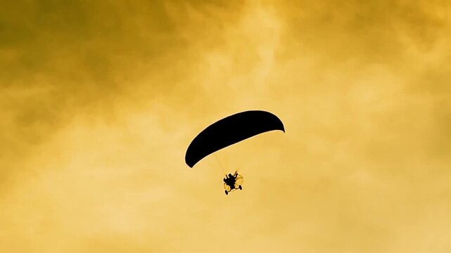 A silhouette of a paraglider soaring through the golden sky. The person appears small against the vast expanse, gliding effortlessly