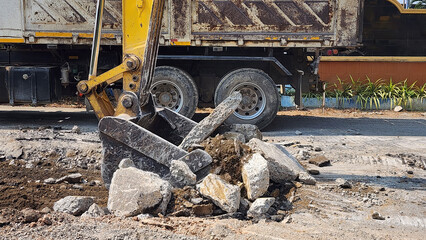 Fototapeta premium Excavator Digging Up Road Surface, Excavator loading broken concrete and soil into a dump truck at a construction site, road demolition and site preparation work