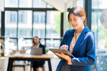 Fototapeta premium A cheerful businesswoman stands in her office, using a digital tablet to work on a financial project.