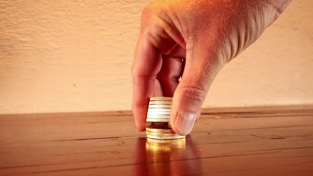 Close-up on hand counting stacked gold coins on wood tabletop, wealth concept