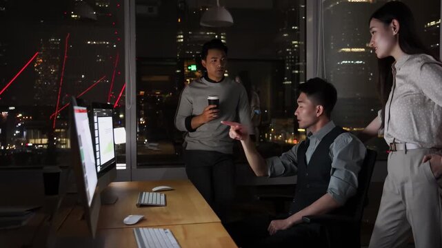 Three male and female business colleague office workers in front of computers late at night creative session, exchanging ideas and solution to meet a project deadline, with city lights in background