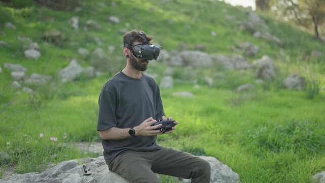 FPV drone pilot wearing goggles and controlling drone flight outdoors in a green forest area.