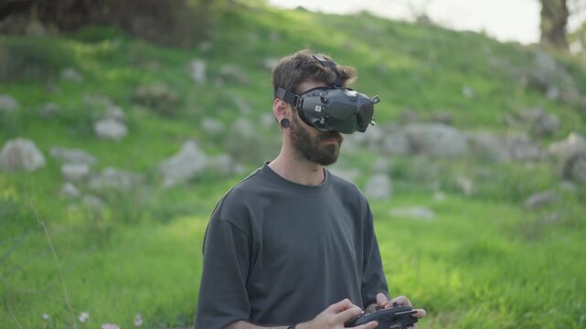 FPV drone pilot wearing goggles and controlling drone flight outdoors in a green forest area.