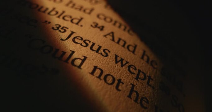 A detailed view of a Bible page highlighting the verse Jesus wept in warm lighting.