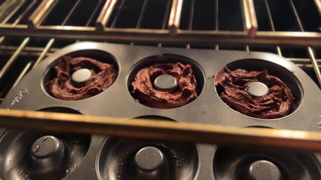 POV shot placing a donut batter tray into a preheated oven during home baking preparation.