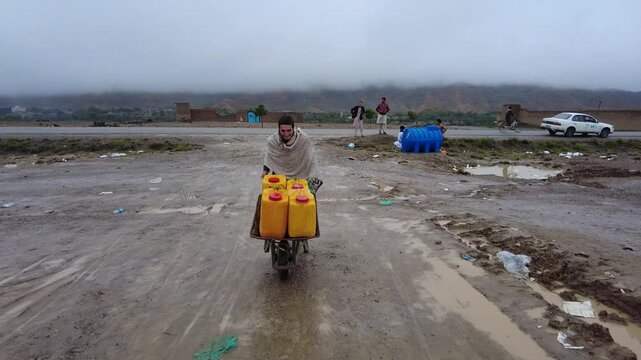 In Khwakhe District of Logar Province, a boy carries water on wheelbarrow in jerrycans in a camp where families have taken shelter after devastating floods forced them to leave their homes.