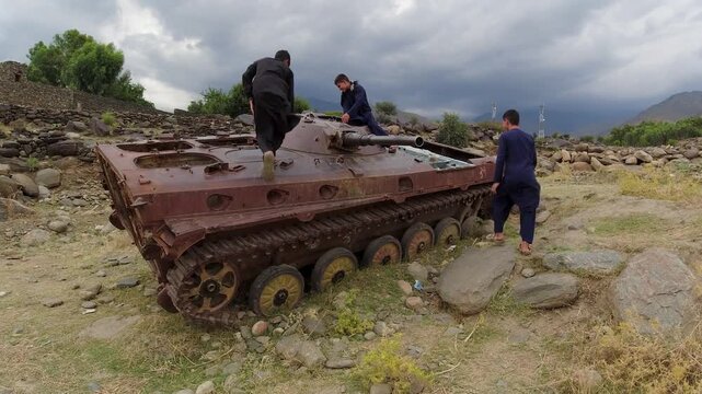 Kids climb a destroyed rusty old military tank Soviet T62 in Afghanistan, near Kabul from Soviet American war in arid mountain landscape, Khogyani. Resilience, marks of war torn country and taliban