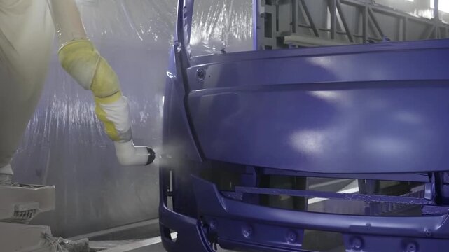 Close-up of a robotic paint sprayer precisely coating the front panel of a blue bus