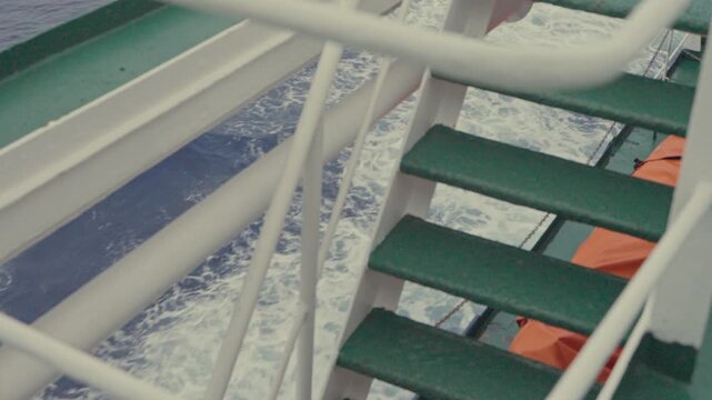 Close-up slow motion shot of green metal stairs and white railings on Antarctic expedition vessel with churning ocean wake visible through deck structure below