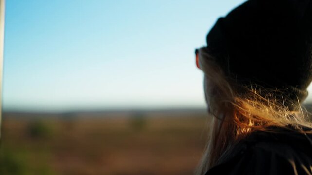 Rear and side shot of a young woman wearing a beanie which indicates a sunny winter day observing the vast landscape from a game vehicle