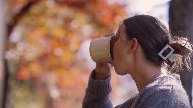 Close up of a woman admiring the fall foliage in her backyard while drinking a cup of coffee