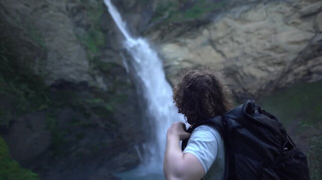 Solo male hiker standing at the Reichenbach waterfall near Meiringen in the Swiss Alps, surrounded by rugged rock, Authentic outdoor adventure footage for hiking, travel and nature in Switzerland