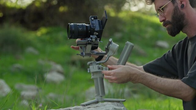 Videographer balancing camera gimbal on a rock while preparing for filming outdoors.