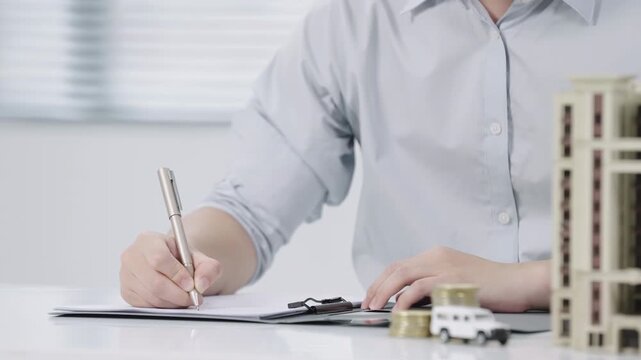 Businessman signing contract, purchase agreement high rise building, car models, stacked coins, symbolizing savings, loans, real estate, automobile investment, insurance, financial security, property
