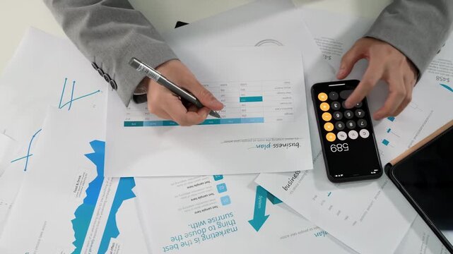 Businesspeople or accountant hand holding pen working calculating with finances paperwork to analyze cost, reviewing financial data reports, calculator about financial reports, investment, economy