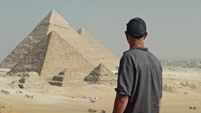 Man from behind, looking out over the legendary Giza Plateau. All three major pyramids are visible: the Great Pyramid of Khufu, the Pyramid of Khafre and the smaller Pyramid of Menkaure.